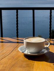 coffee cup on table with scenic view lake atitlan antigua guatemala blue water sunny volcano crater pond outdoor travel tourism adventure getaway cappuccino late milk cafe restaurant flavor santa cruz