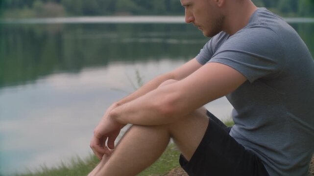 A slow tilt-down shot focusing on a person sitting by a lake as the camera descends.