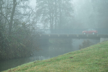 Betonbr&uuml;cke mit rotem Fahrzeug  im Nebel vor kahlen B&auml;umen an der Flutmulde nahe der Ermsm&uuml;ndung in Neckartenzlingen