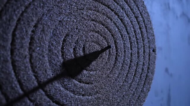 Round coiled rope mat on blue surface with speckled texture, diagonal shadow across rings with dust