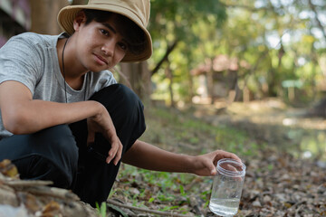 A boy, geared up with a cream boonie hat passionately exploring tiny life forms contained within a clear plastic bottle. Igniting curiosity and the spirit of scientific discovery.