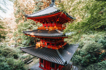 A vibrant red Japanese pagoda stands amidst lush green trees