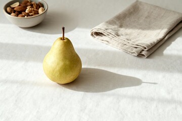 A minimalist food photo: a single pear and a small bowl of nuts