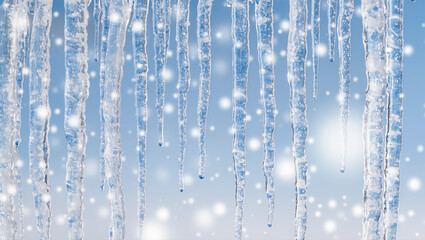 Christmas winter scene with transparent icicles hanging against a soft blue background and falling snow. Frozen cold weather concept with sparkling ice details.