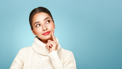 Portrait of young happy beautiful woman smiling and looking away, isolated on blue background in a warm white sweater. Concept of winter promo sale