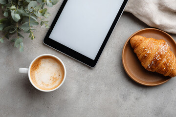 Top-down view of coffee, pastry, and a tablet with blank screen on a concrete table surface