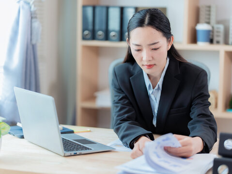 An Asian businesswoman is working on her laptop with financial documents, reviewing financial analysis reports and managing accounting tasks. - Powered by Adobe