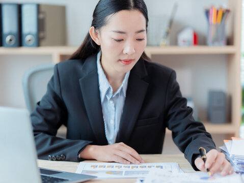 An Asian businesswoman is working on her laptop with financial documents, reviewing financial analysis reports and managing accounting tasks. - Powered by Adobe