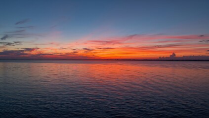 Fototapeta premium Vivid sunrise illuminating a broad river with reflected clouds and gentle water ripples, suitable for editorial header backgrounds