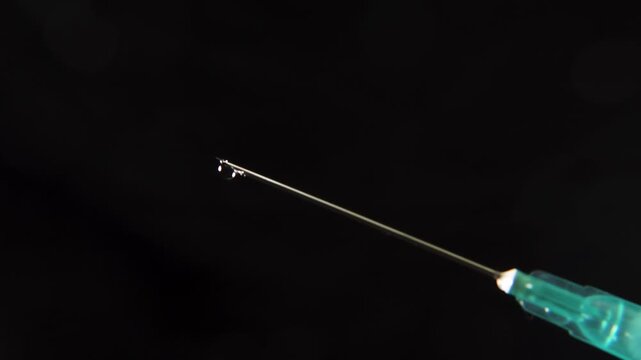 Syringe needle tip dripping liquid against a black background, highlighting medical precision, vaccination themes, and healthcare concepts.
