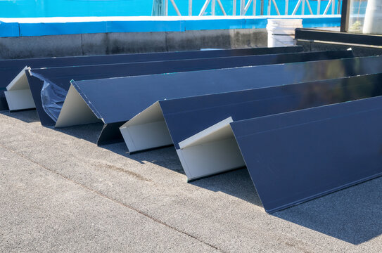 Roof metal flashing or coping installation. Custom sheet metal corners ready for installation on modified bitumen roofing system. Defocused waterproofing membrane behind. Selective focus.