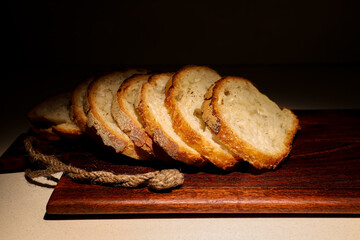 Rustic homemade bread slices arranged on a textured wooden board, warm highlights emphasizing the crust and crumb, minimalist dark background for gourmet food presentation.