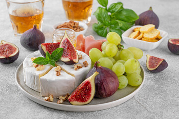 Camembert, bree cheese, walnuts, fresh figs, grapes, prosciutto and honey on a plate on a concrete background. Charcuterie plate. Top view