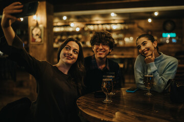 Three friends sit at a wooden table in a warmly lit bar, smiling as one takes a selfie. Glasses of beer and casual conversation capture a fun night out together.
