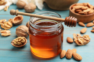 Honey in jar, nuts and dipper on light blue wooden table, closeup