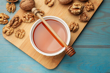 Honey in bowl, walnuts and dipper on light blue wooden table, flat lay