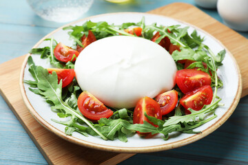 Delicious burrata cheese with tomatoes and arugula on light blue wooden table, closeup