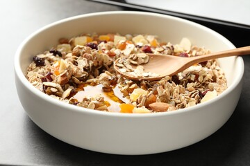 Making granola. Bowl with oat flakes, honey and dried fruits on grey table, closeup