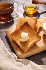 Fresh toasted bread slices with butter, honey and tea on grey table, closeup