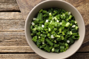 Bowl with cut green onions on wooden table, top view. Space for text