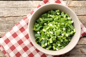 Bowl with cut green onions on wooden table, top view