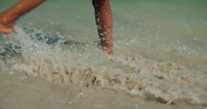 Person, legs and splash at beach with waves for summer holiday, travel adventure or weekend break. Woman outdoor, feet and walk in ocean water for tropical vacation, wellness or connection to nature.