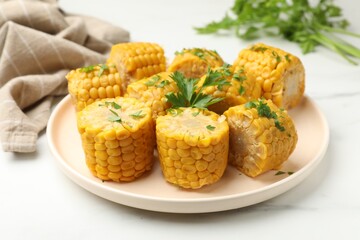 Pieces of boiled corncobs with parsley on white marble table, closeup