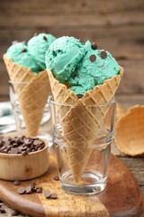 Tasty mint chocolate chip ice cream in waffle cones on wooden table, closeup