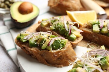 Delicious bruschettas with avocado, onion and microgreens served on light table, closeup