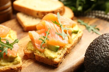 Tasty bruschettas with salmon, arugula and avocado on table, closeup