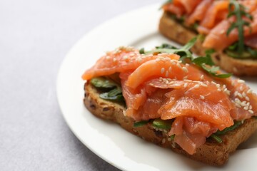 Tasty bruschettas with salmon, arugula and avocado on light grey table, closeup