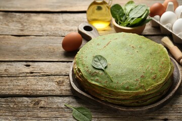 Tasty spinach crepes, brush and ingredients on wooden table, closeup. Space for text