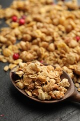 Tasty granola with dried fruits and spoon on black table, closeup
