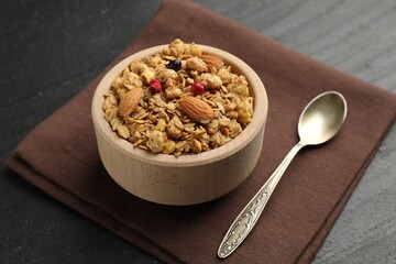 Tasty granola with dried fruits and nuts in bowl on black table, closeup