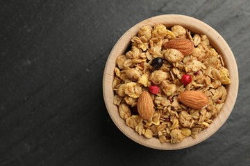 Tasty granola with dried fruits and nuts in bowl on black table, top view. Space for text