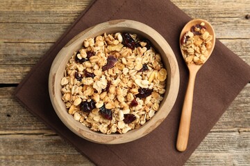 Tasty granola with dried fruits in bowl and spoon on wooden table, flat lay