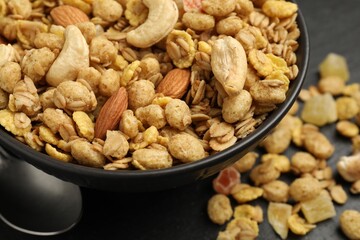 Tasty granola with dried fruits and nuts in bowl on black table, closeup