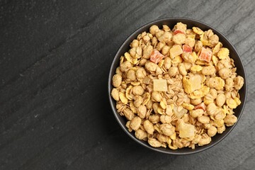 Tasty granola with dried fruits in bowl on black table, top view. Space for text