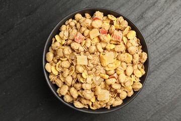Tasty granola with dried fruits in bowl on black table, top view