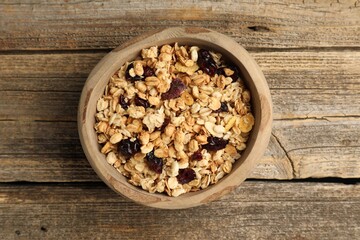 Tasty granola with dried fruits in bowl on wooden table, top view