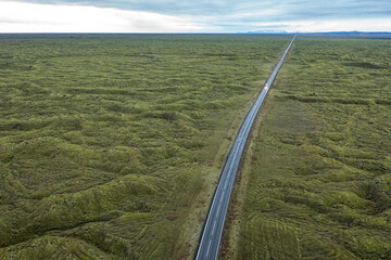 Road through valley of volcanic lava with moss, mountains on horizon. Drone photo. Southern Iceland.