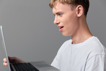 Young man gazes at a laptop screen with a surprised expression in a clean studio setting, showcasing casual tech use, online learning, and digital exploration during work or study.