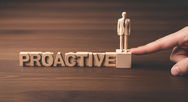 Wooden blocks spell proactive with a small businessman figure standing atop the final block as a finger gently pushes the base on a dark wood surface