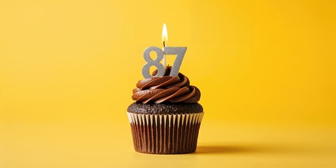 Chocolate cupcake adorned with a single birthday candle on a yellow backdrop, celebrating a 87th birthday milestone