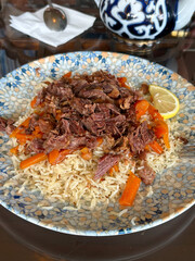 Traditional uzbek pilaf or plov with shredded braised meat and carrots served on a patterned ceramic plate with a slice of lemon