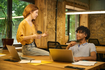 Woman standing, holding a phone and looking at a colleague
