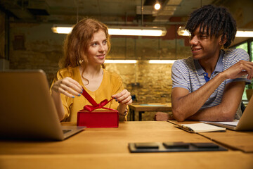 Man and woman sitting, discussing a red gift box