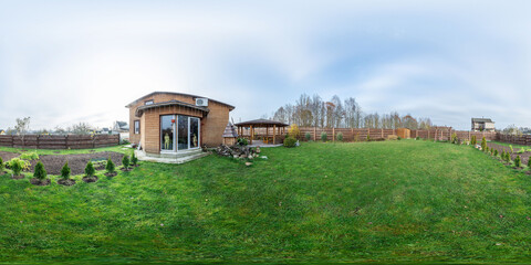 Seamless spherical HDRI panorama with a 360-degree angle view of a green lawn and a house in the background. Green lawn, green paddock. VR content.