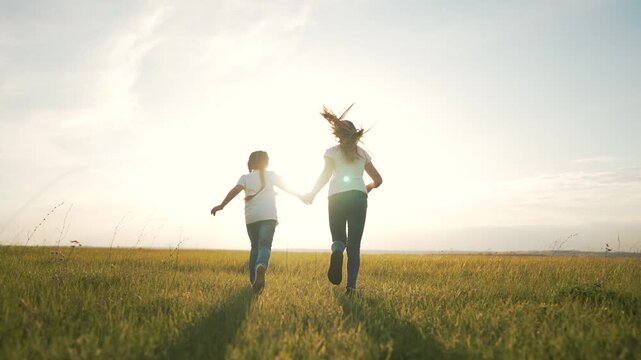 Running through sunlit grass field mother and daughter holding hand backlit by sunset in summer running across open meadow with joyful movement warm light natural outdoor bond playful energy
