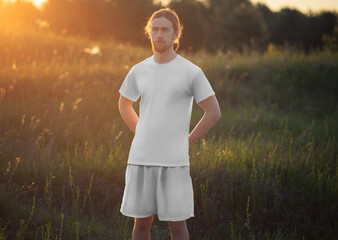 Mockup of a white t-shirt, shorts for a man with long hair, a beard, on the background of nature, sunset, front view, for design, branding.